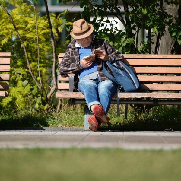 A senior man enjoying leisure reading on a park bench with a relaxed ambiance.