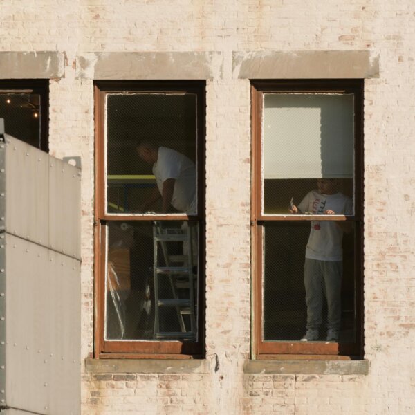 Men seen through windows working on interior renovations in a New York City building.